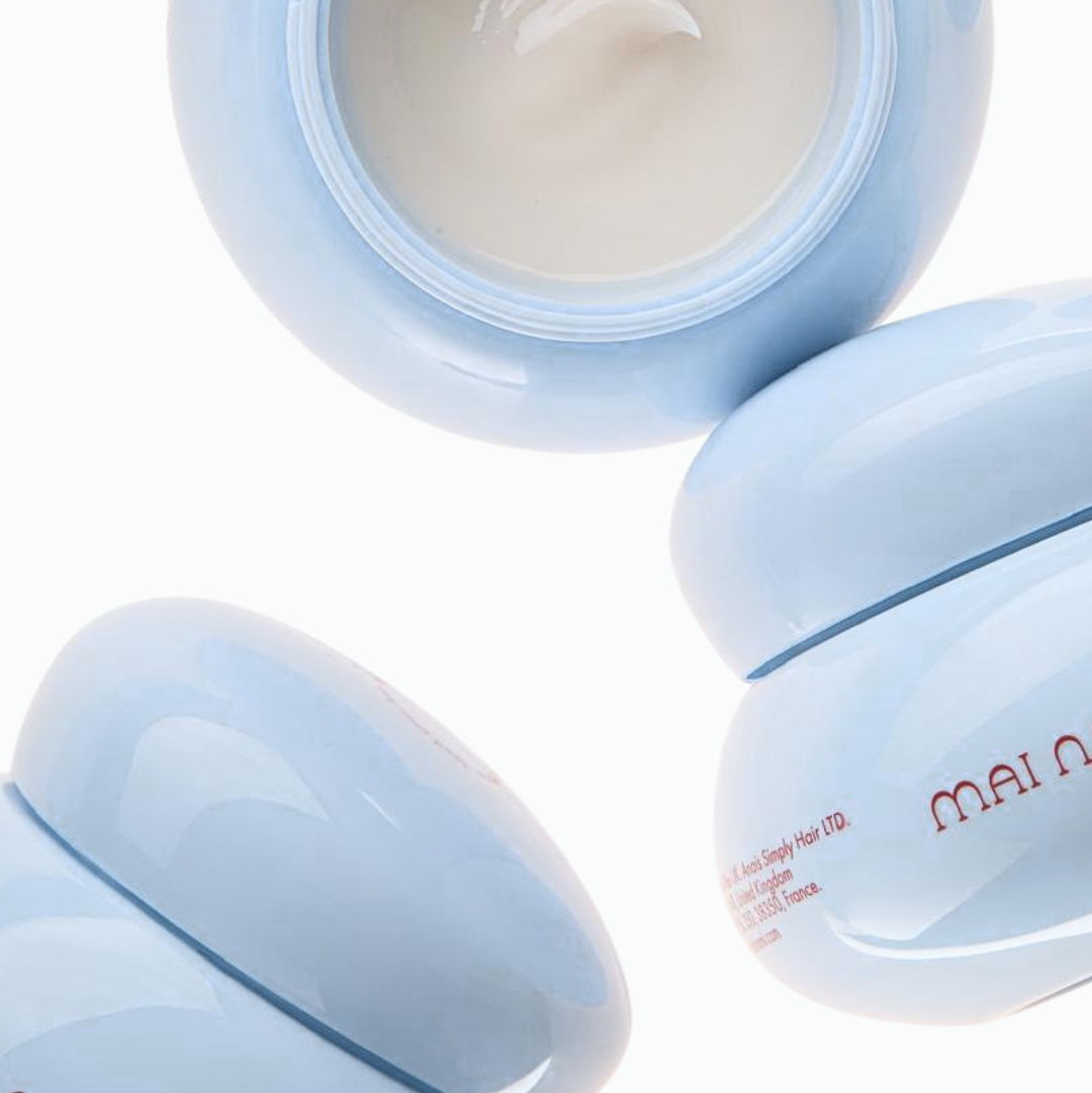 Stacked Mai Nami Hair Pudding pots with a wide-tooth comb on a deep blue backdrop